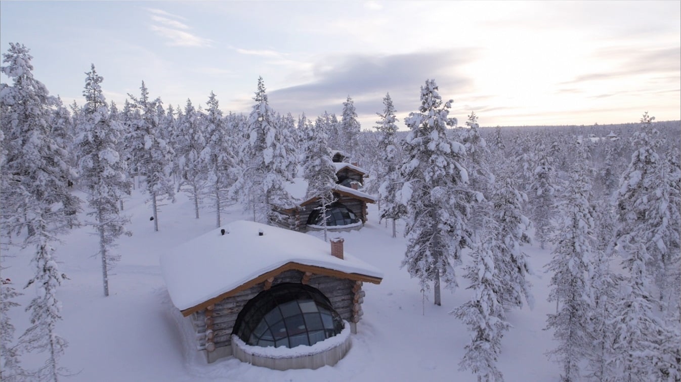 Villaggio di igloo in legno circondato da foresta innevata in Lapponia, Finlandia, al tramonto