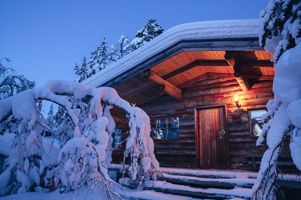 Baita di legno illuminata al tramonto circondata da abeti innevati in Lapponia