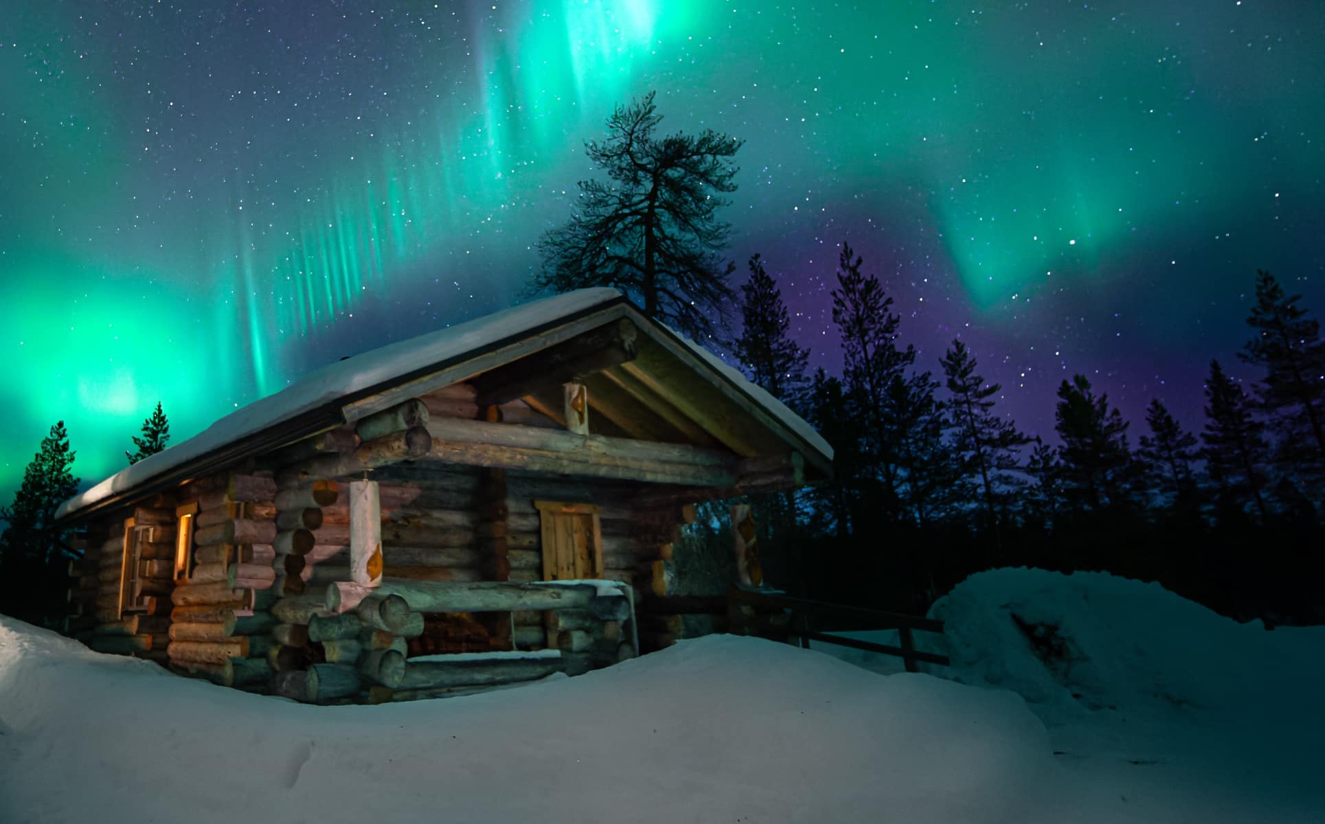 Baita in legno illuminata dall'aurora boreale verde tra boschi di conifere innevati in Lapponia