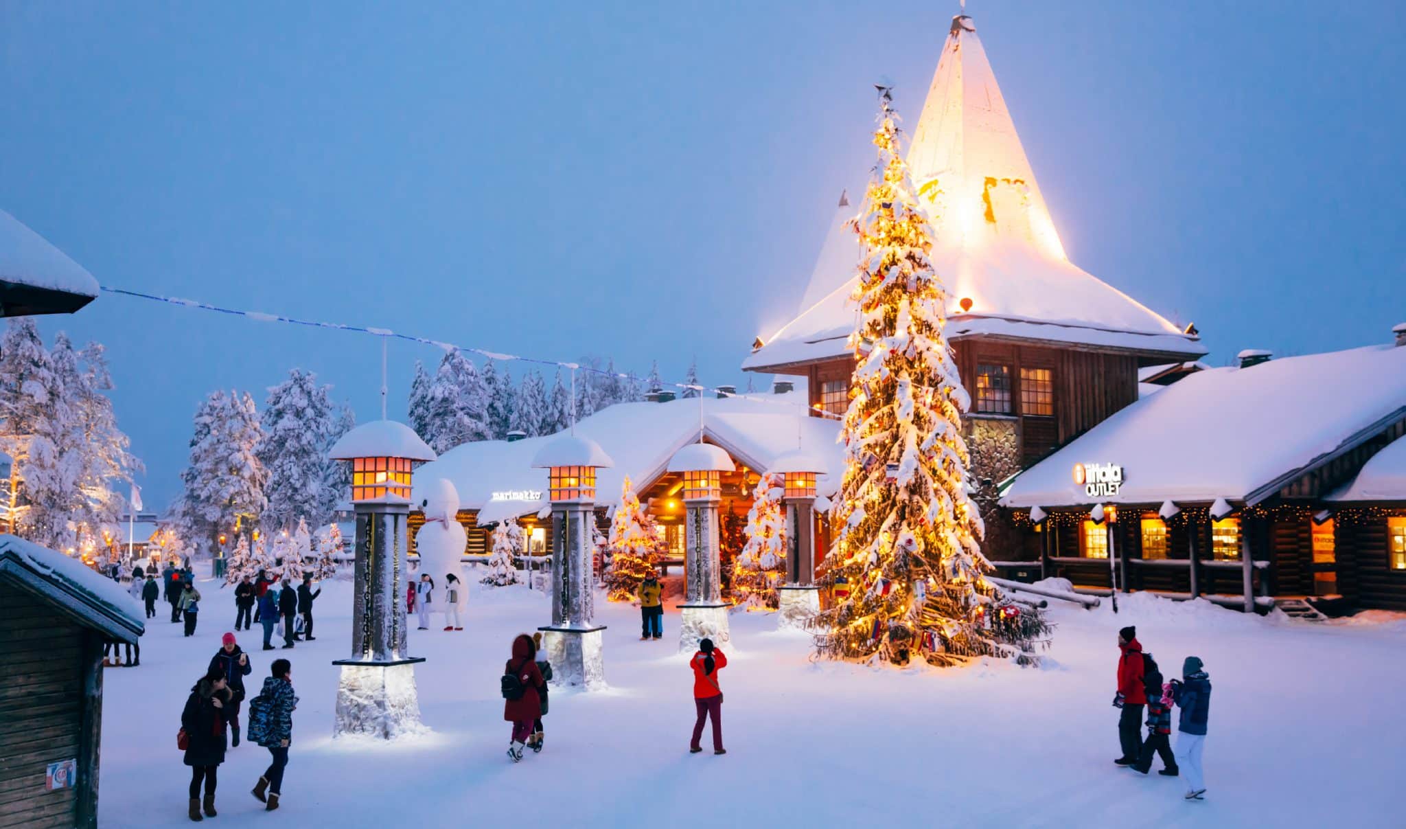 Villaggio di Babbo Natale a Rovaniemi con decorazioni natalizie, alberi innevati e turisti al tramonto invernale
